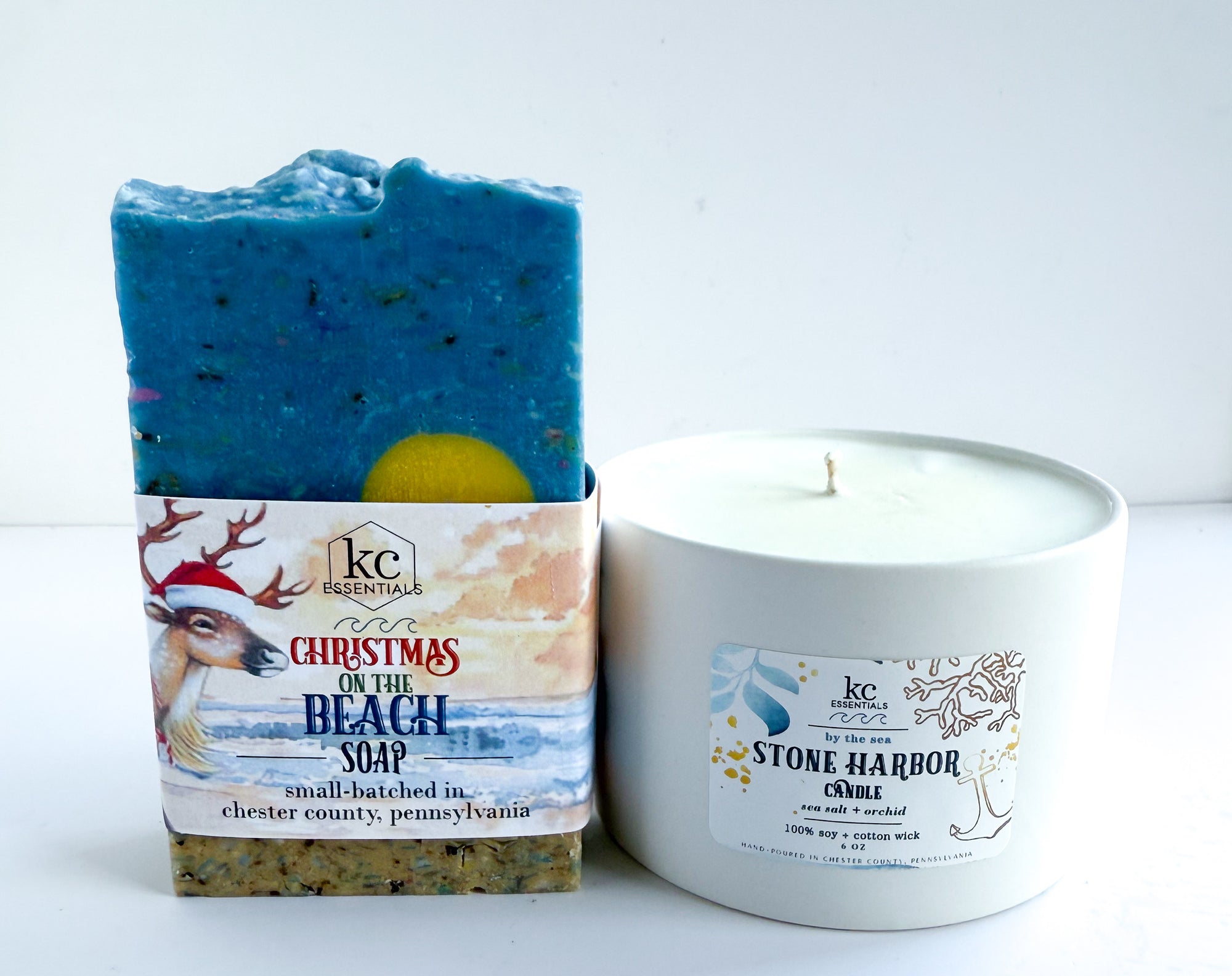 Blue soap bar with packaging and a white candle on a light background, christmas on the beach soap, all natural hand soap, soap bar, stone harbor beach, new jersey, jersey beaches, 100% soy candles, christmas gift ideas, festive, holiday